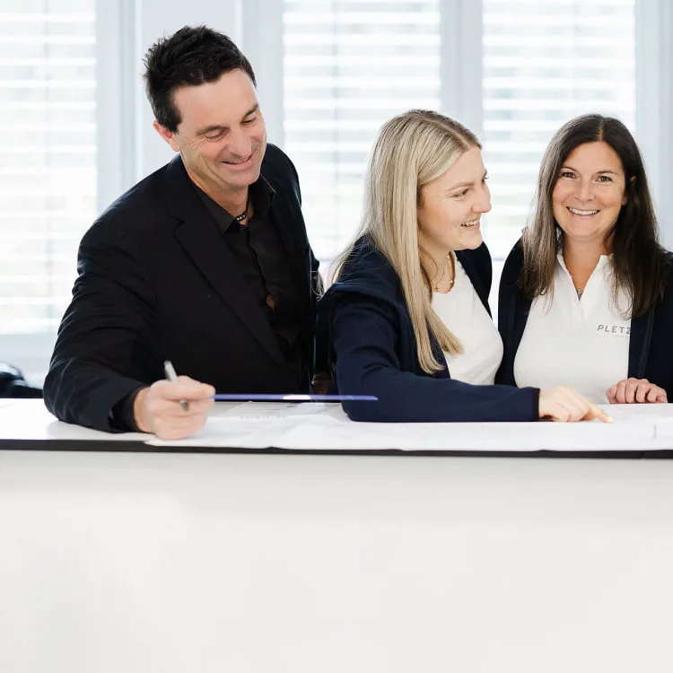 Team von Pletzer Immobilien bei einer gemeinsamen Besprechung – drei Mitarbeitende lächeln und arbeiten zusammen an einem Dokument.